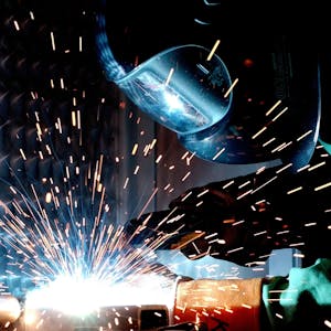 A focused welder works with metal in an industrial setting, creating vibrant sparks.