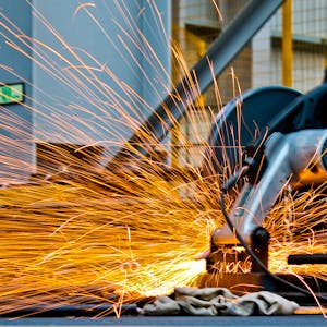 A worker operates a grinder cutting metal, creating a vibrant display of sparks in an industrial setting.