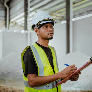 Asian construction worker in a factory setting, using a clipboard for inspection tasks in Banting, Malaysia.