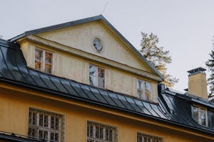 Close-up of a vintage house with a rustic yellow facade and black metal roof in an autumn setting.