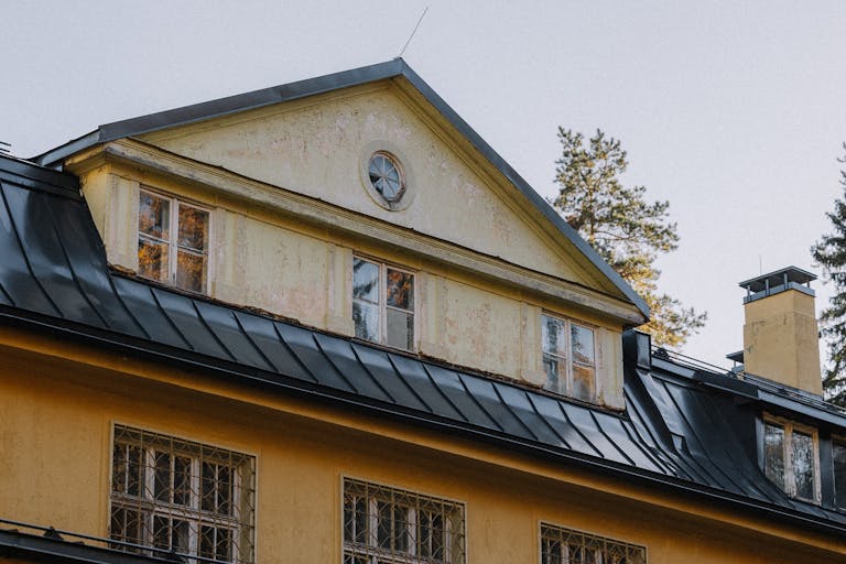 Close-up of a vintage house with a rustic yellow facade and black metal roof in an autumn setting.