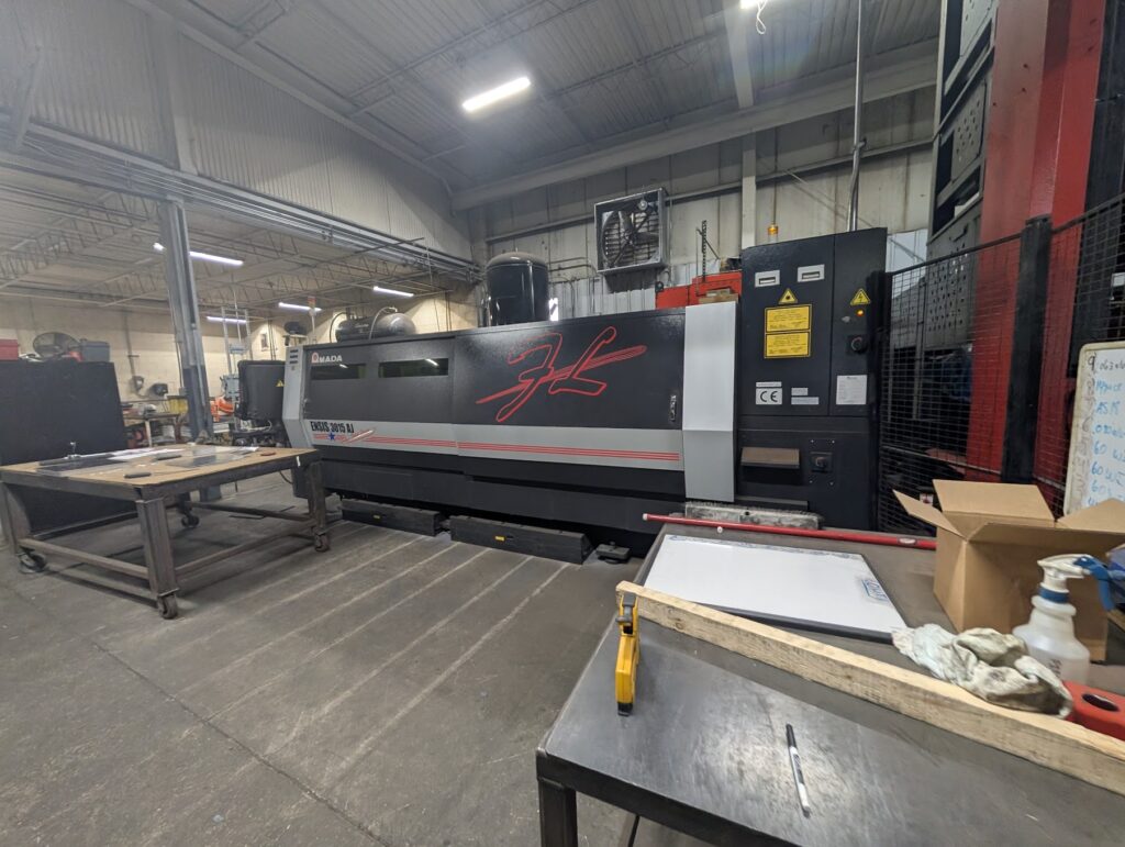 Operator-side view of an Amada ENSIS 3015 AJ fiber laser cutting machine on a shop floor
